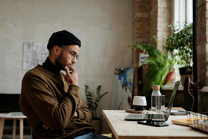 Man in casual attire at a desk, looking at a laptop, contemplating an expensive trip to visit a long-distance girlfriend.