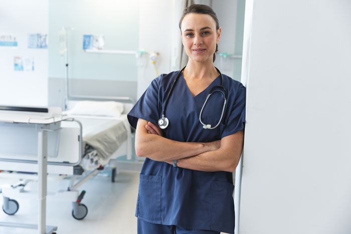 Nurse standing confidently in a hospital room, ready to assist patients with professional care.