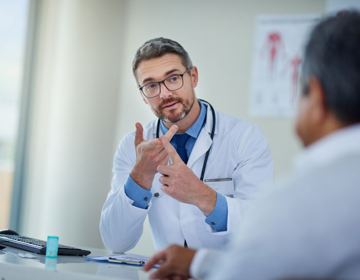Doctor in discussion with a patient, gesturing with hands, wearing a white coat and stethoscope.