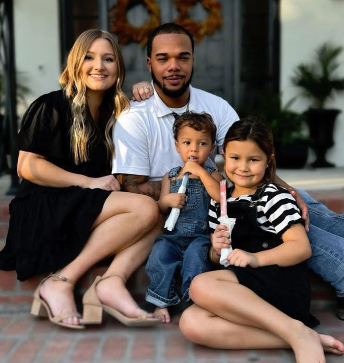 A family on steps, smiling together. Young boy, known as 'Okay Baby,' holds a popsicle, remembered fondly.