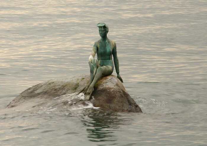 Statue of a mermaid on a rock in the sea, illustrating a disappointing FOMO-induced experience for tourists.