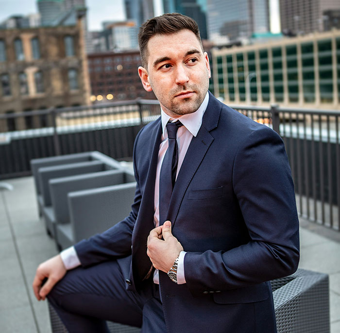A man in a suit on a rooftop, embodying out-of-touch luxury with cityscape in the background.