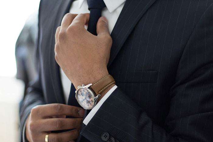 Man in suit adjusting tie, wearing a watch, symbolizing rich lifestyle choices.