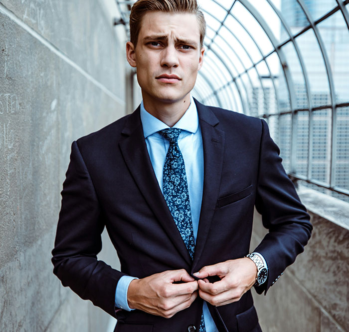 Young man in a suit with a blue tie, outdoors, conveying a sense of wealth and style.