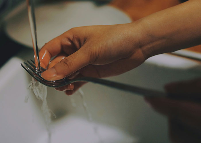 A hand washing a fork under running water in a kitchen sink, reflecting everyday tasks.