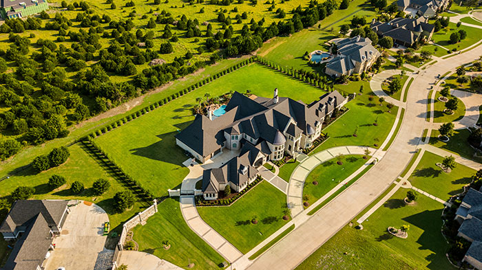 Aerial view of a luxurious mansion in a wealthy neighborhood, showcasing rich lifestyle with expansive green lawns.