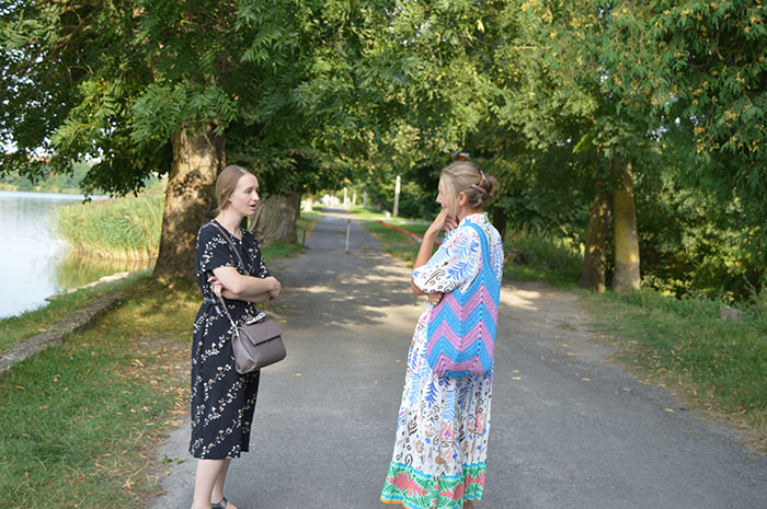 Two women in casual dresses talking on a tree-lined path, representing rich people’s perspectives.