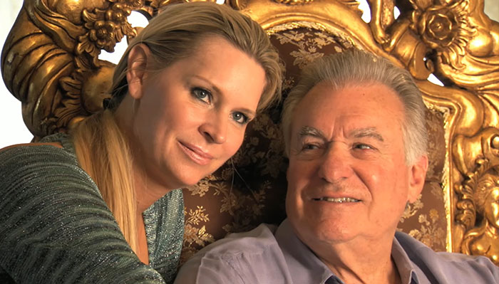 A smiling couple sitting on an ornate chair, representing out-of-touch perspectives of wealthy individuals.