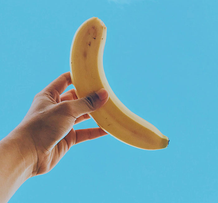 Hand holding a banana against a clear blue sky, symbolizing out-of-touch perspectives.
