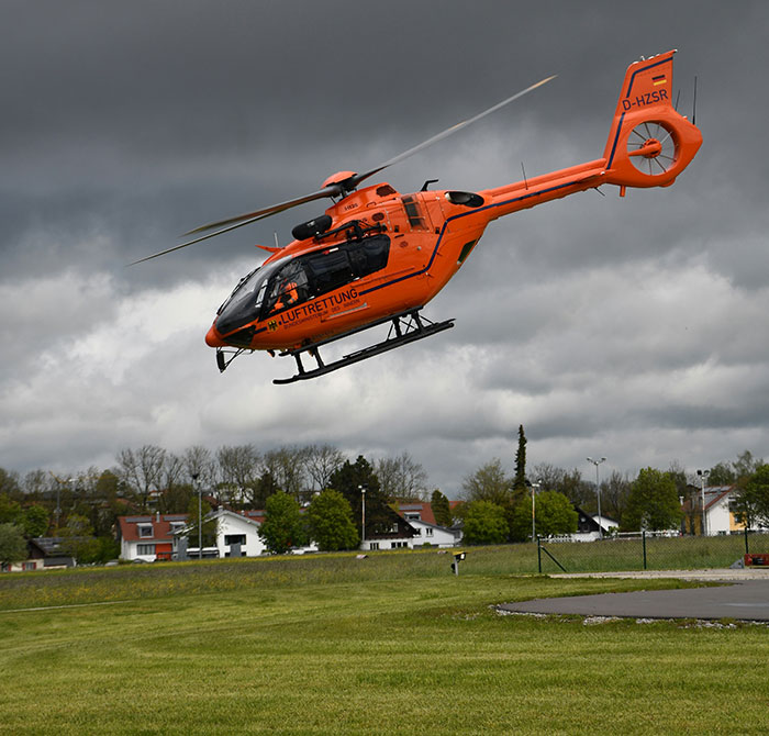 Orange helicopter landing in a grassy field under cloudy skies, symbolizing out-of-touch luxury.