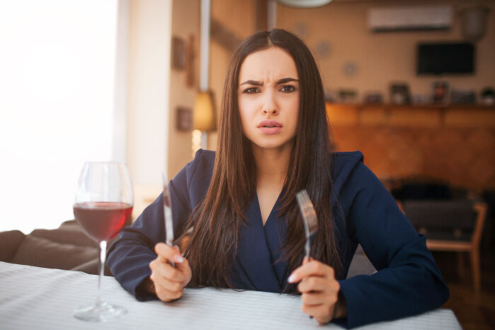 Young woman in a blue blazer sitting at a table with cutlery, showing frustration, reflecting changes after the pandemic.