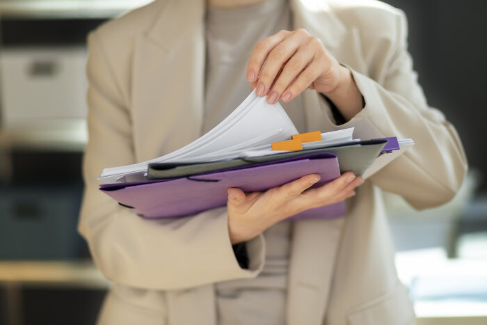 Person flipping through documents in a beige blazer, illustrating usual things that ended with the pandemic and changed forever.