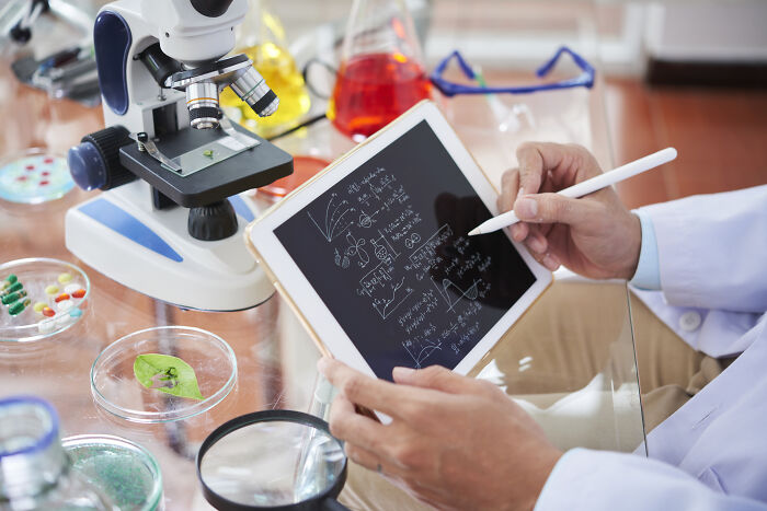 Scientist using a tablet to analyze data with microscope and lab equipment, illustrating changes after the pandemic.