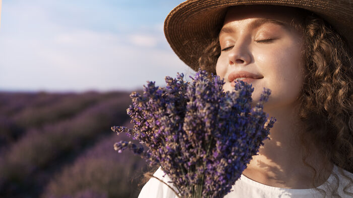 Young woman in a hat enjoying lavender scent outdoors, representing usual things that ended with the pandemic.