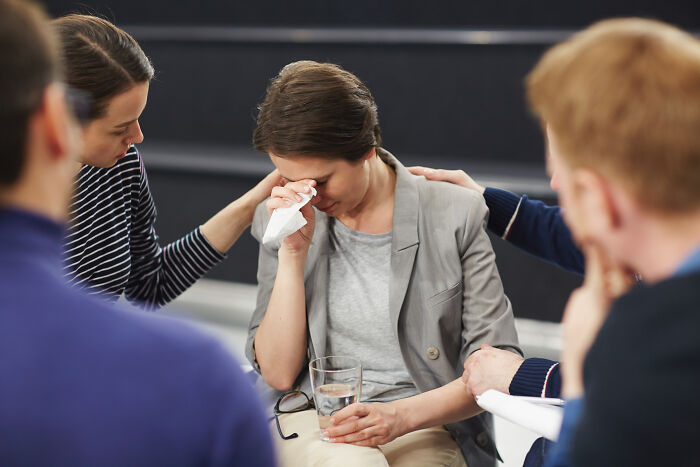 Woman crying during group therapy session, people comforting her, reflecting usual things changed by the pandemic impact.