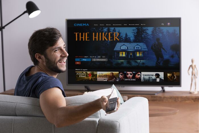 Man smiling on couch holding remote, watching streaming service at home, illustrating usual things ended with the pandemic changes.