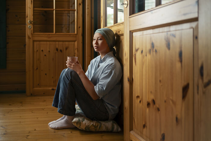 Young woman sitting indoors holding a cup, reflecting on usual things that ended with the pandemic and their lasting impact.