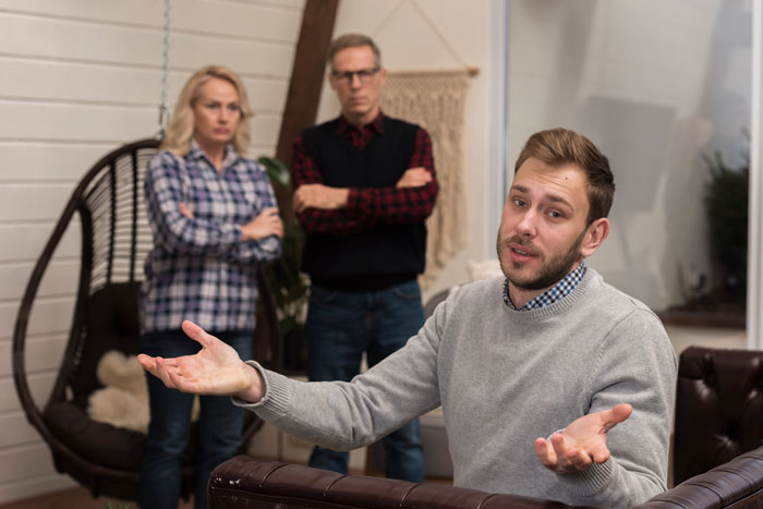 Son looks frustrated while parents seek babysitting help during a family visit. Son looks frustrated while parents seek babysitting help during a family visit.