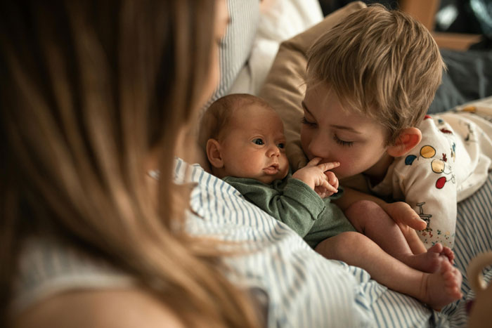 A young boy gently touches a newborn baby's hand, with the mother watching, conveying a family visit moment. A young boy gently touches a newborn baby's hand, with the mother watching, conveying a family visit moment.