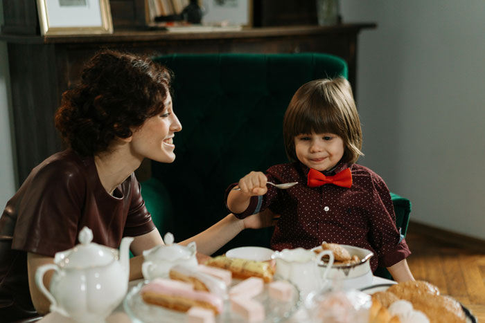 Mother and son at a table with desserts and tea, smiling and enjoying family time together indoors. Mother and son at a table with desserts and tea, smiling and enjoying family time together indoors.