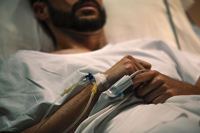Man in hospital bed with IV, illustrating impacts of parents' decisions to kick out kids at 18.