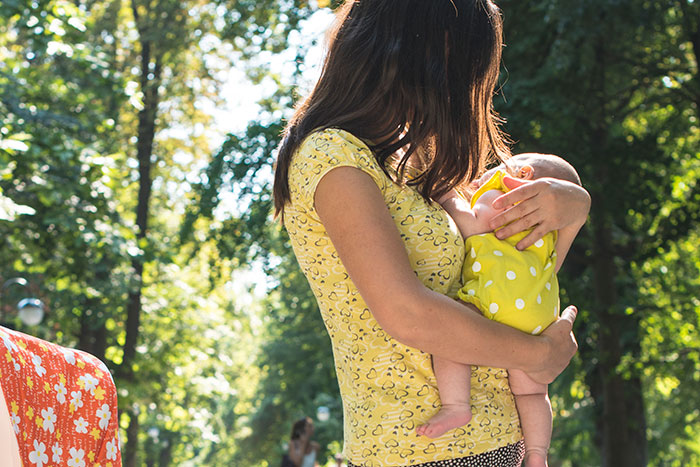 Woman holding baby in a park, wearing yellow outfits, under sunlight.