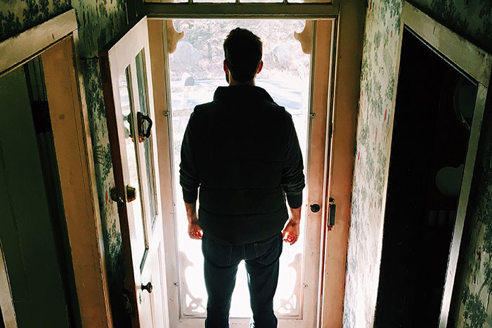 Person standing at a doorway, contemplating parents’ decision to kick kids out at 18.