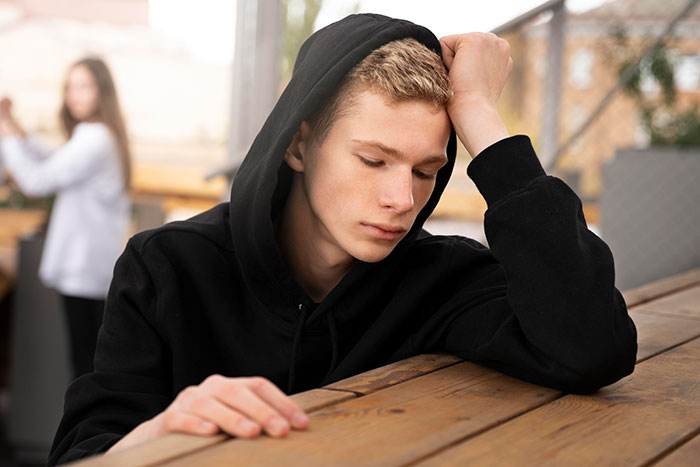 Teen in black hoodie looking pensive, symbolizing thoughts on parents kicking kids out at 18.