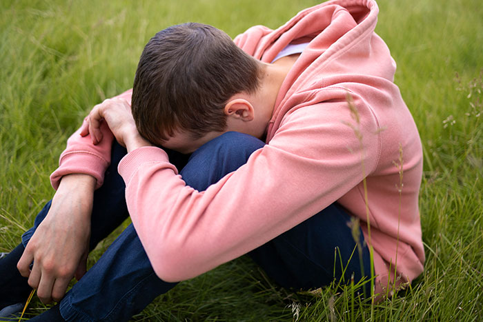 Young person in a pink hoodie sitting in a field, reflecting on being kicked out by parents at 18.