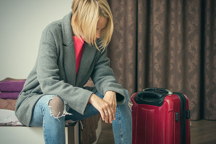 Woman sitting with suitcase, contemplating experiences of being kicked out at 18.