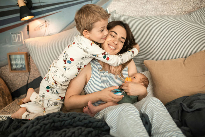 Mother cuddling her children in bed, illustrating family dynamics during babies’ nap time. Mother cuddling her children in bed, illustrating family dynamics during babies’ nap time.