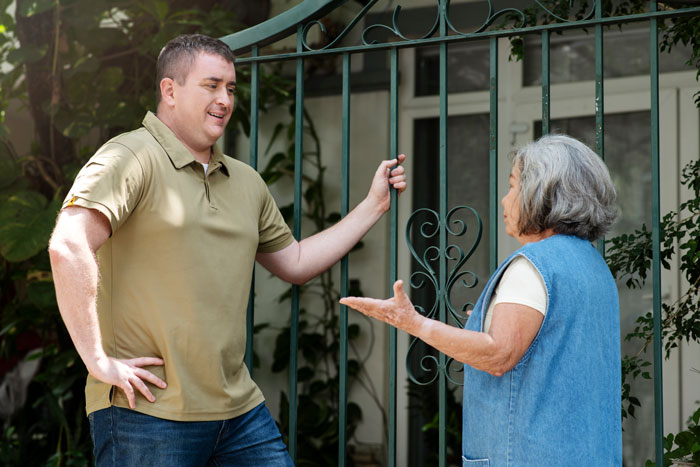 Man and older woman talking at a gate outside a house, discussing surprise visit concerns during babies' nap. Man and older woman talking at a gate outside a house, discussing surprise visit concerns during babies' nap.