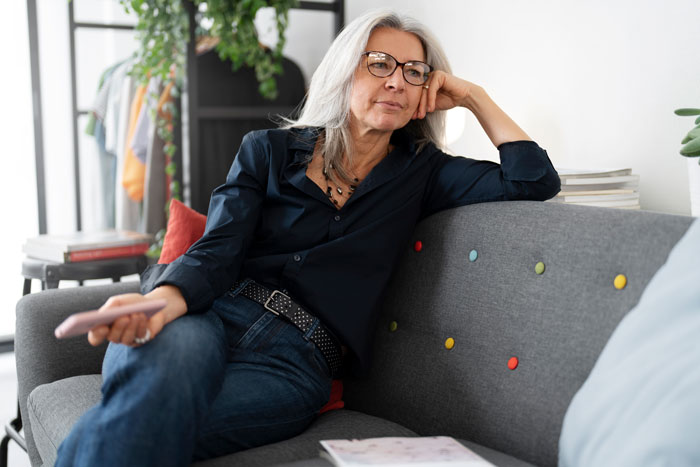 Woman sitting on a sofa, looking thoughtful, relating to couple and in-laws visit disagreement. Woman sitting on a sofa, looking thoughtful, relating to couple and in-laws visit disagreement.