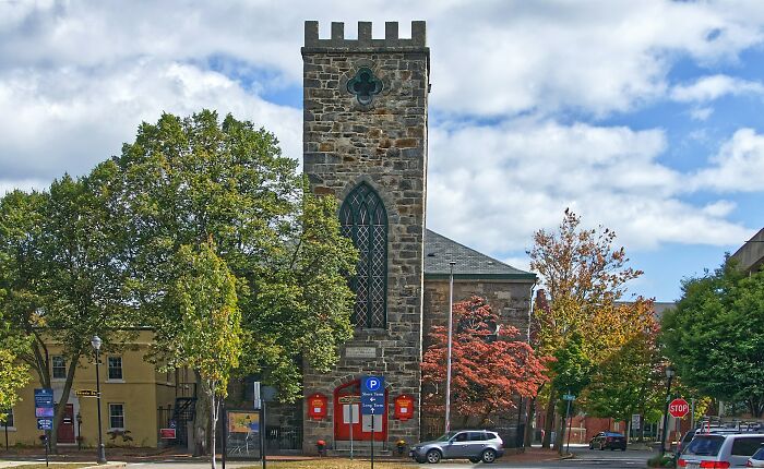 Historic stone church with tall tower in an island town, surrounded by trees and cars.