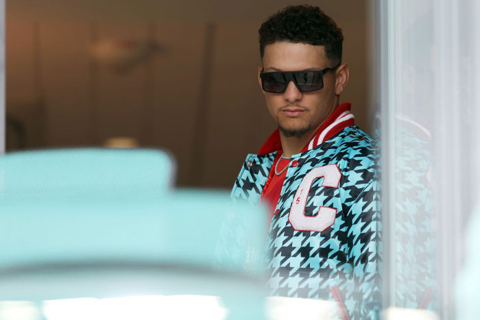 Patrick Mahomes in a houndstooth jacket and sunglasses, symbolizing a rise in net worth and power moves.