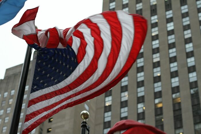 American flag waving in front of a tall building, reminiscent of scenes from 30 years ago.