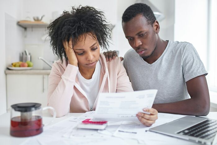 Couple looking stressed over paperwork in kitchen, possibly related to hiding pets from landlord.