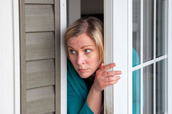 Woman looks cautiously out a door, concerned about strangers claiming to be half-siblings.