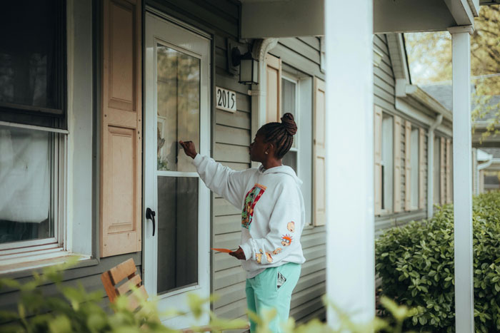Woman answering door to strangers claiming to be half-siblings, outside suburban house.