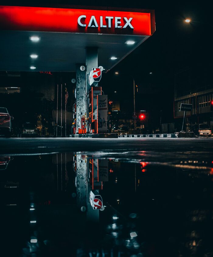 Gas station at night with vibrant reflections in a puddle, resembling a real life glitch in the matrix.