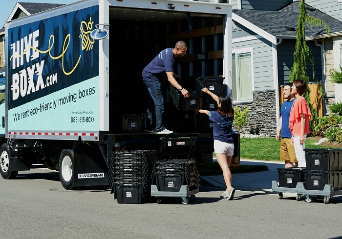People loading identical black boxes into a moving truck, resembling a glitch in the Matrix.
