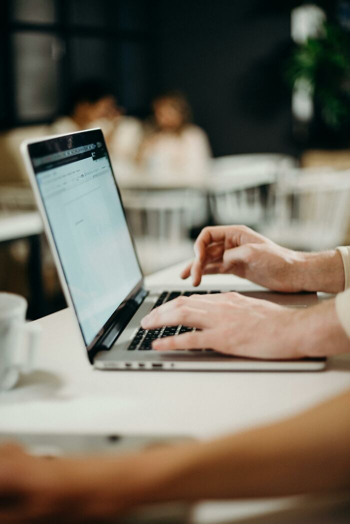 Hands typing on a laptop in a cafe setting, demonstrating creative ways to use ChatGPT.
