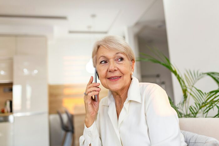 Elderly woman using a smartphone, sitting in a bright living room, highlighting unhinged ways people use ChatGPT.