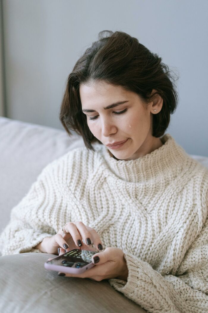 Woman using phone, exploring unhinged ways to utilize ChatGPT while relaxing on a couch.