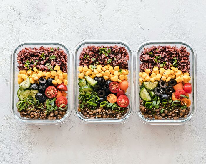 Three meal prep containers with vibrant veggies and grains arranged in neat rows, showcasing unhinged creativity in food styling.
