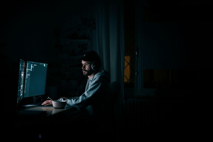 A person in a dimly lit room using ChatGPT on a computer, wearing headphones and focused on the screen.