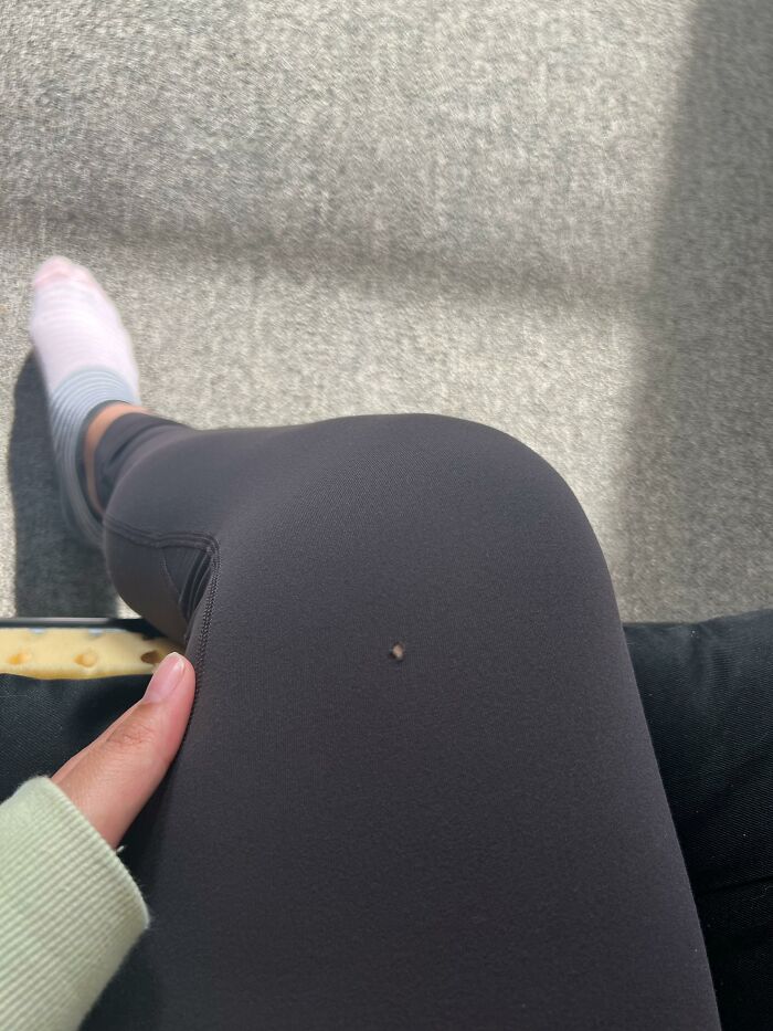 Finger pointing at a small hole in black leggings, referencing brands and items people refrain from using.