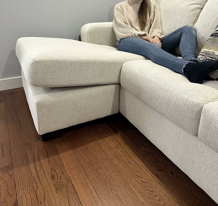 Person sitting on a white couch in a living room with wooden flooring.