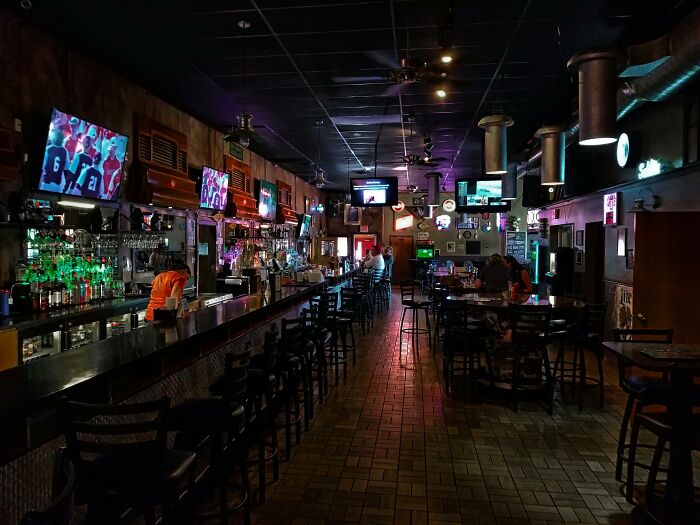 Dimly lit bar interior featuring a long counter, multiple TVs, and patrons dining, representing brands and stores theme.