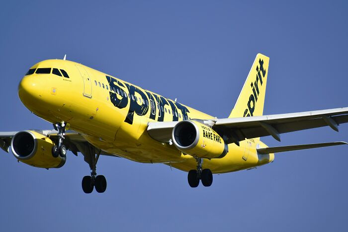 Yellow Spirit Airlines airplane in flight against a clear blue sky.